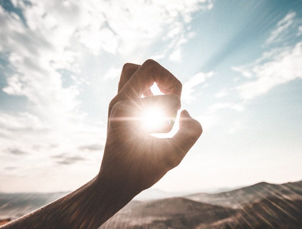 photography of sun glaring through the hole of finger